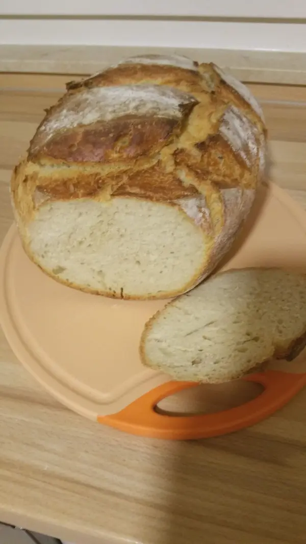 Ein rundes, goldbraunes Joghurtbrot liegt auf einem Schneidebrett, daneben liegt eine Scheibe, frisch geschnitten.