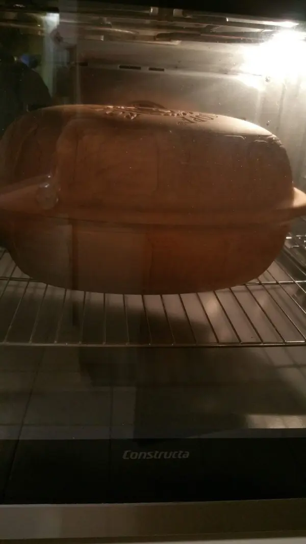 Ein Römertopf mit frisch gebackenem Joghurtbrot wird im Ofen auf einem Rost gebacken, umgeben von warmem Licht.