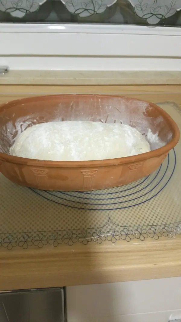 Ein Römertopf steht auf einem Holzbrett und enthält eine dicke, weiße Joghurtmasse, bereit zum Backen.