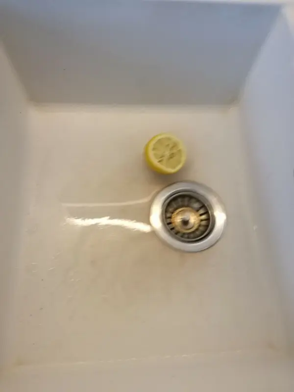 Ein Kunststein-Waschbecken mit braunen Flecken, in dem eine halbe Zitrone zur Reinigung liegt, in einer hellen Umgebung.