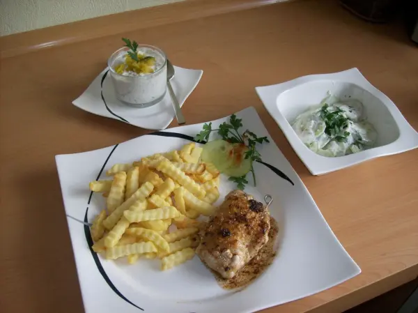 Auf einem Teller liegt ein Schweinesteak, umgeben von knusprigen Pommes frites und zwei kleinen Schalen mit Dip in einem hellen Raum.