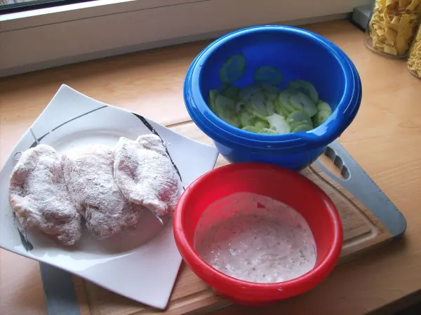 Saftige Schweinesteaks liegen auf einem Teller, während in bunten Schüsseln frischer Salat und eine cremige Füllung vorbereitet werden.