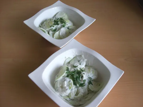 Zwei Schalen mit cremigem griechischem Joghurt, garniert mit frischen Kräutern, auf einem Holzuntergrund platziert.