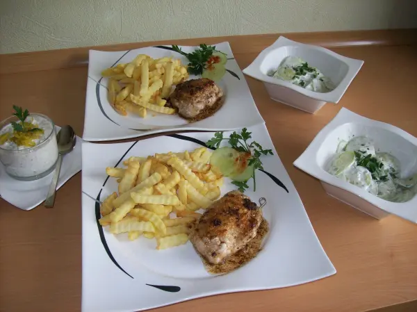 Zwei Teller mit gefüllten Schweinesteaks und Pommes frites, daneben köstlicher Joghurt-Dip in Schalen.
