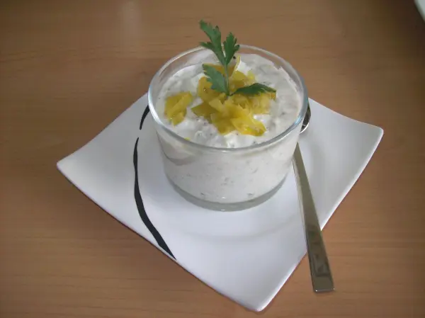 Ein Glas mit griechischem Joghurt, garniert mit Früchten und frischer Petersilie, steht auf einem weißen Teller.