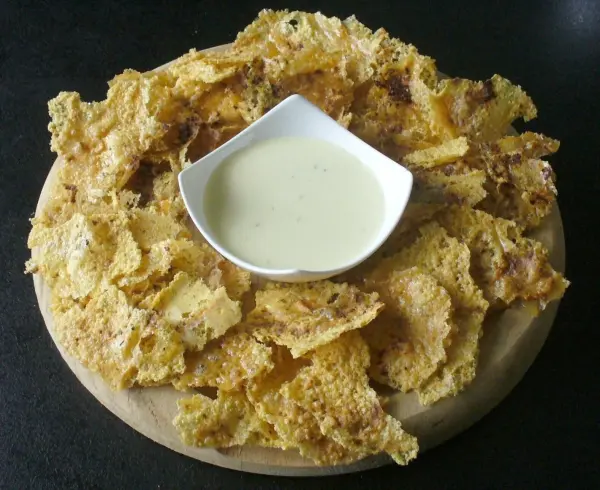 Käsechips sind knusprig und goldbraun, serviert auf einem Holzbrett mit einer kleinen Schüssel Dip in der Mitte.