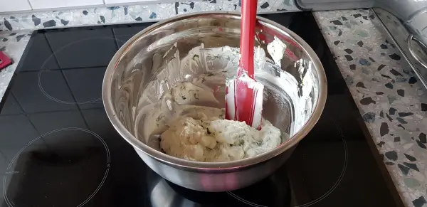 Ein roter Silikonteigschaber rührt in einer Schüssel mit Teig auf einem Herd, um die Mischung gleichmäßig zu verteilen.