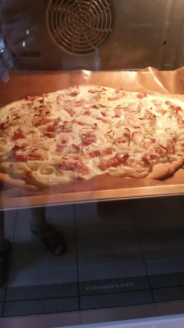 Ein frisch gebackener Elsässer Flammkuchen liegt auf einem Blech im Ofen und verbreitet köstlichen Duft in der Küchente.