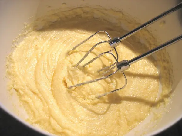 Eine Rührschüssel enthält eine glatte, helle Teigmischung für Schoko-Himbeer-Muffins, während ein Mixer darin rührt.