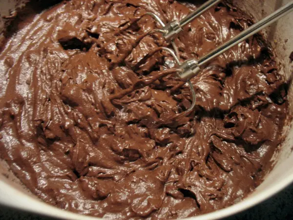 Dunkler, cremiger Schokoladenteig ruht in einer Schüssel, während die Rührgeräte bereit zum Mixen sind, um Muffins zu backen.