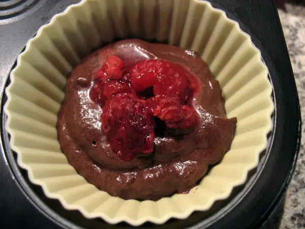 Schokoladenteig mit frischen Himbeeren in einer Muffinform, bereit zum Backen in einer modernen Küche.