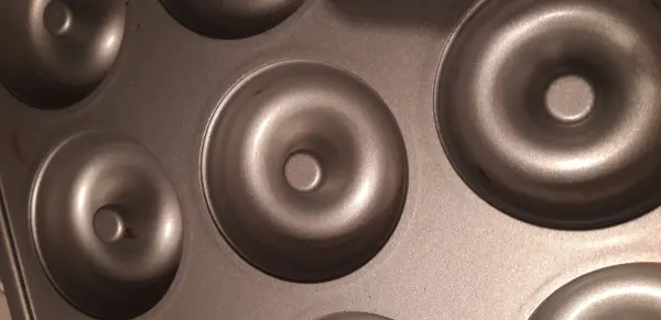 Eine Donut-Form liegt bereit, um Bananen-Apfel-Donuts ohne Zucker zu backen, auf einer dunklen, flachen Oberfläche.