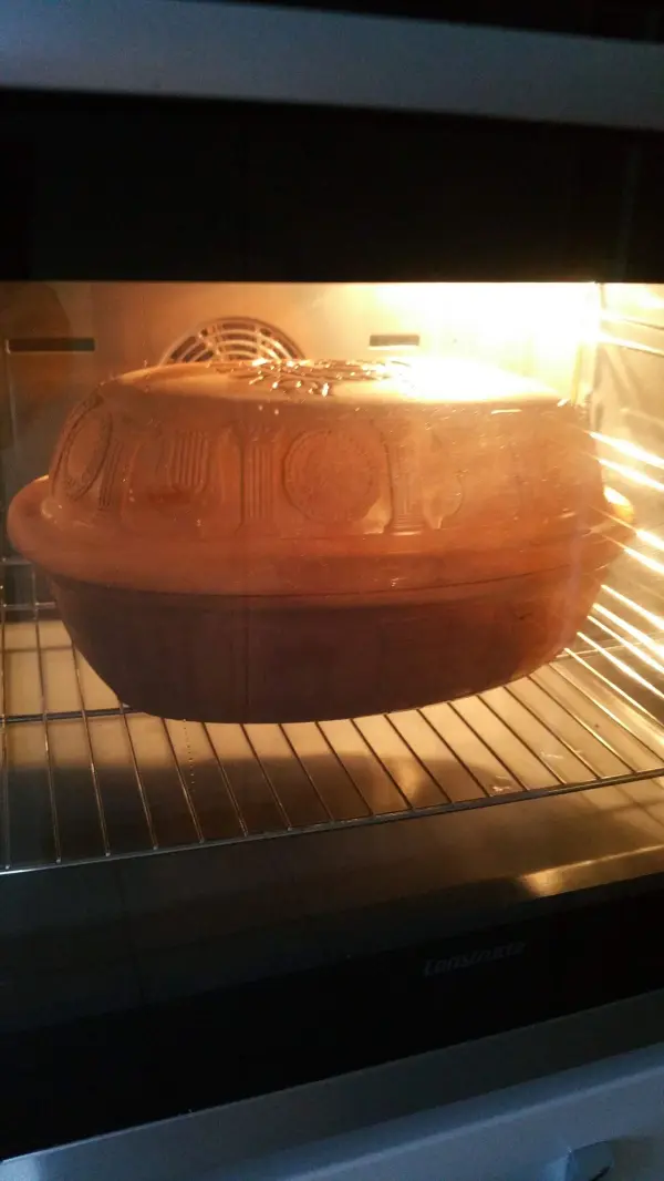 Ein Römertopf befindet sich im Ofen und backt Dinkel-Roggenbrot, umgeben von warmem, hell erleuchtetem Licht.