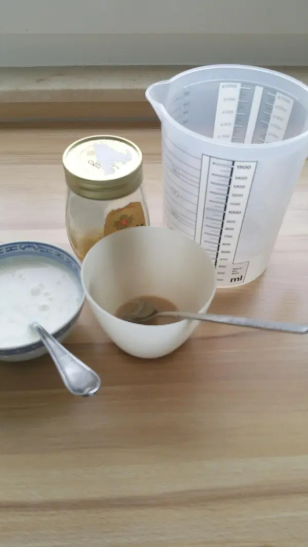 Eine Schüssel mit Dinkel-Roggenbrot-Zutaten steht auf einem Tisch, während Honig und ein Messbecher daneben platziert sind.