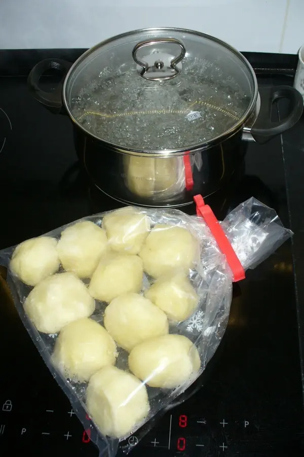 Eine Tüte mit gefrorenen Kartoffelknödeln liegt neben einem kochenden Topf auf dem Herd, bereit zum Kochen.