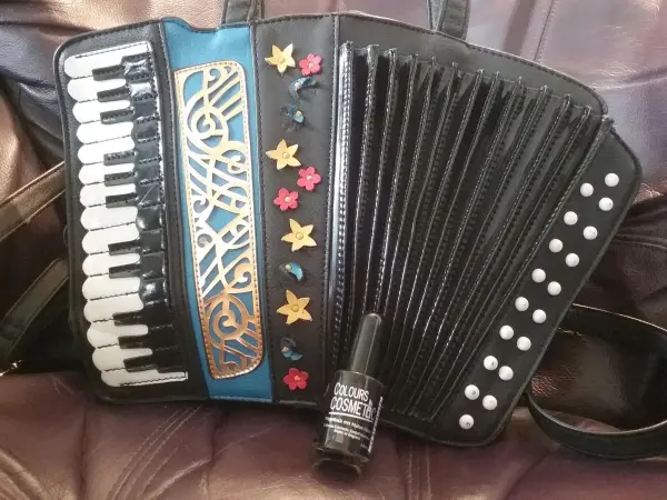 Eine schwarze Kunstledertasche im Design eines Akkordeons liegt auf einem weichen, beigen Hintergrund.