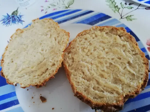 Zwei aufgeschnittene Joghurtbrötchen liegen auf einem blauen, gemusterten Teller auf einem Tisch.
