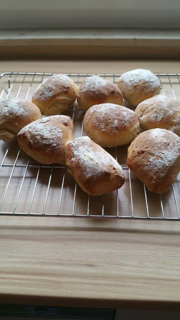 Warmen Joghurtbrötchen liegen auf einem Gitter zum Abkühlen, umgeben von einer hellen Holzoberfläche.