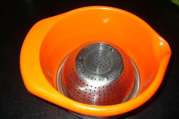 Eine orangefarbene Schüssel mit einem Metallsieb, in dem frische Leber abtropfen kann, steht auf einer dunklen Oberfläche.