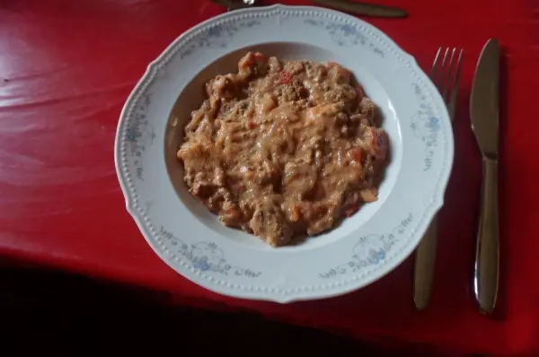 Eine reichhaltige Hacksuppe liegt in einer eleganten Porzellantasse auf einem roten Tisch, umgeben von Besteck.
