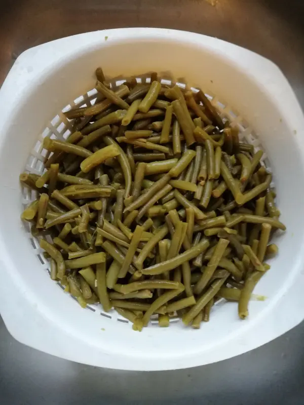 Grüne Bohnen liegen in einem weißen Sieb, während sie abtropfen. Sie sind bereit für den Bohneneintopf mit Äpfeln.