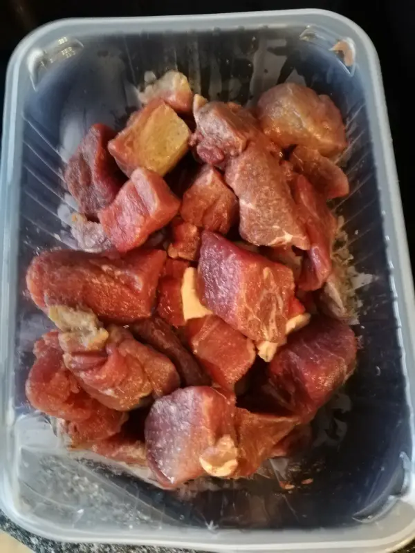 In einem Behälter liegt rohes Fleisch, bereit für die Zubereitung eines Bohneneintopfs mit Äpfeln.