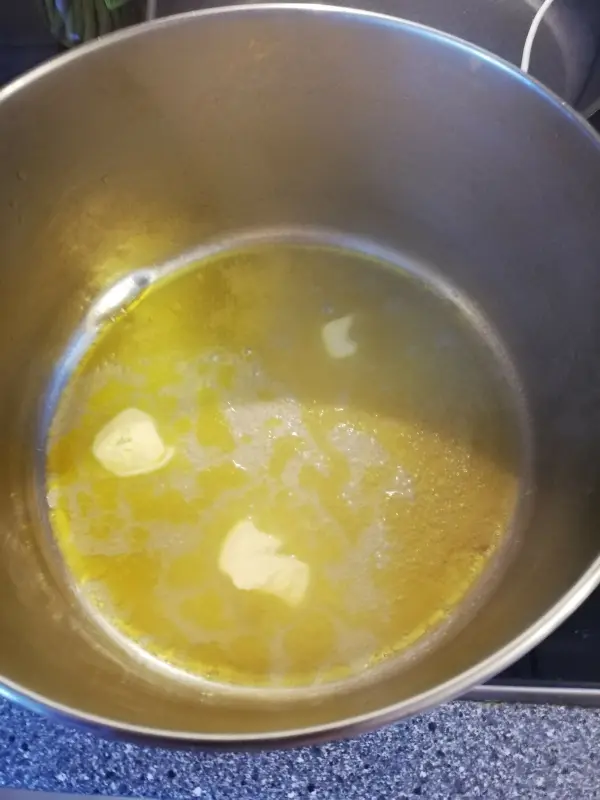 In einem großen Topf schmilzt Butter in einer gelblichen Flüssigkeit, bereit für den Bohneneintopf mit Äpfeln.