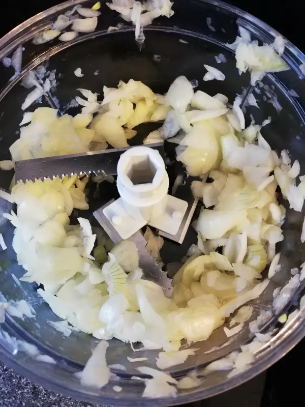 Fein gehackte Zwiebeln liegen in einer Küchenmaschine, bereit für die Zubereitung eines herzhaften Bohneneintopfs mit Äpfeln.