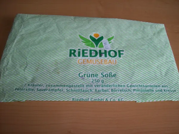 Eine Verpackung mit der Beschriftung "RIEDHOF Grüne Soße" liegt auf einem Tisch. Sie enthält Informationen zur Zubereitung.