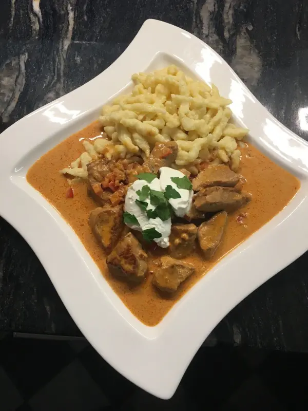 Ein herzhaftes Paprika-Rahm-Gulasch mit zarten Fleischstücken, serviert mit Spätzle auf einem eleganten Teller.