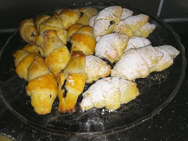 Frisch gebackene Schmalzkipferl liegen auf einer Glasplatte, einige mit Puderzucker bestäubt, bereit zum Servieren.
