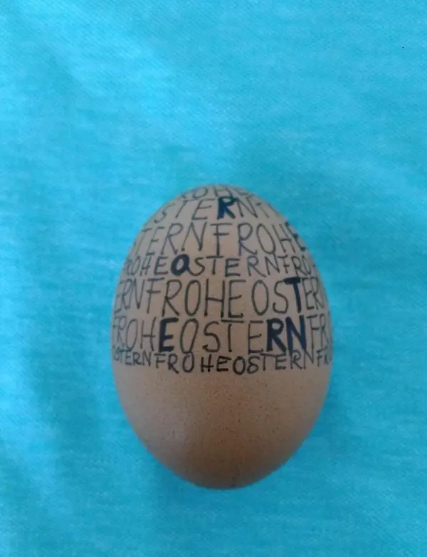 Ein braunes Ei ist mit der Schrift "FROHE OSTERN" detailreich verziert, auf einem türkisen Hintergrund platziert.