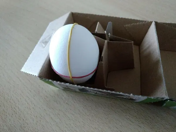Ein Ei liegt in einer Kartonverpackung, umgeben von Pappfächern, die zur Stabilität dienen.