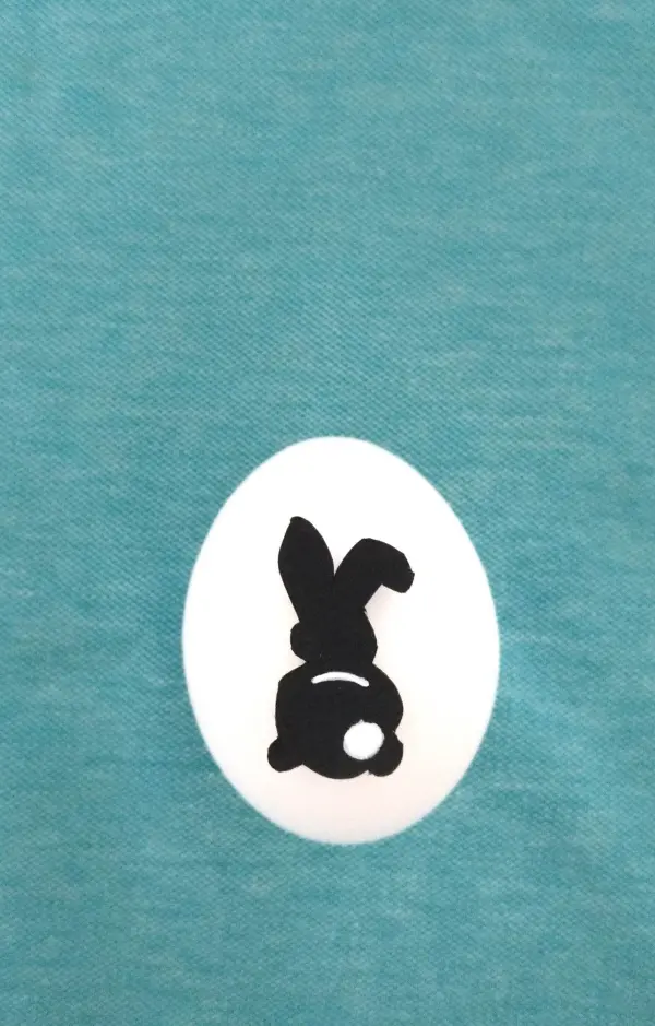 Ein weißes Ei mit einem schwarzen Hasenmotiv steht auf einem türkisfarbenen Hintergrund, ideal zum Eier Verzieren zu Ostern.
