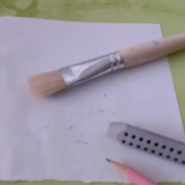 Ein Pinsel liegt auf einem weißen Blatt Papier, umgeben von einem Bleistift und einem Radiergummi, bereit zum Eier verzieren.