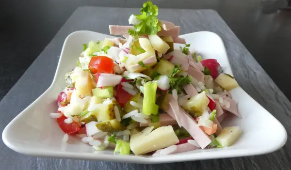 Ein bunter Wurstsalat wird auf einem weißen Teller präsentiert, umgeben von frischen Gemüsezutaten und Kräutern.