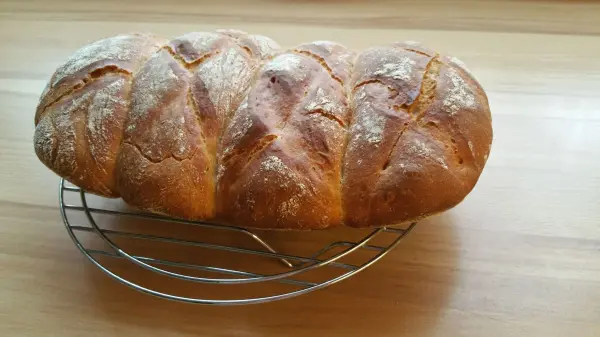 Ein goldbraunes Brot mit knuspriger Kruste ruht auf einem Gestell aus Metall und zeigt eine schöne, geflochtene Oberfläche.
