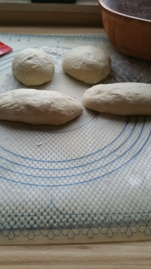 Vierlinge aus Brot liegen auf einer bemehlten Unterlage, bereit zum Backen im Römertopf, um knusprige Kruste zu entwickeln.