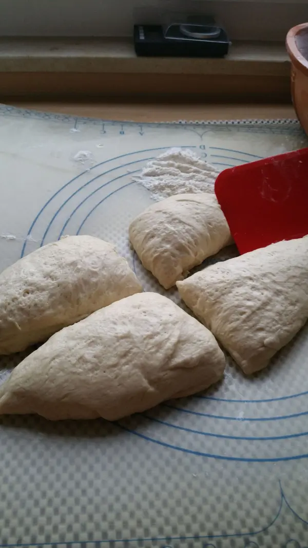 Vierlinge aus Brotteig liegen auf einer Holzunterlage, während ein Schaber daneben liegt, bereit zum Formen.