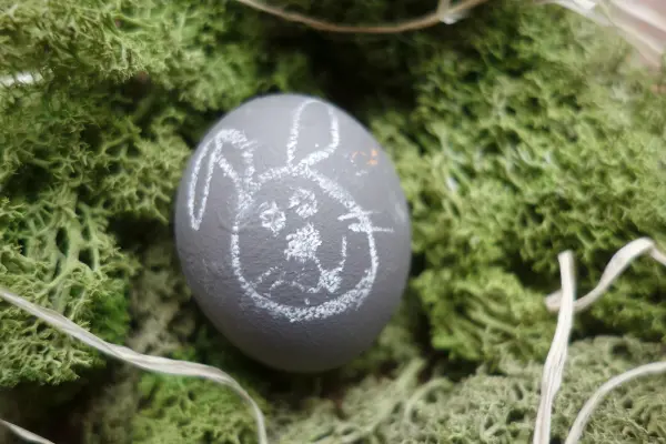Ein graues Osterei liegt auf grünem Moos und zeigt mit Kreide einen Hasen. Es ist liebevoll dekoriert für Ostern.