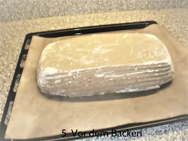 Ein Laib Sauerteig-Roggenmischbrot liegt auf einem Backblech, bereit zum Backen, umgeben von einer Küchenoberfläche.