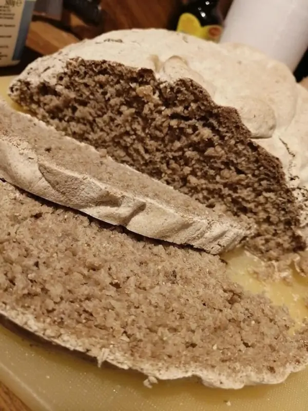 Ein aufgebackenes Sauerteig-Roggenmischbrot liegt angeschnitten auf einem Brett, die krustige Oberfläche zeigt die innere, luftige Textur.