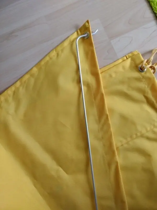 Ein gelbes Stoffstück liegt auf einem Tisch, während ein gebogener Draht neben ihm bereitliegt, um einen Windschutz zu gestalten.