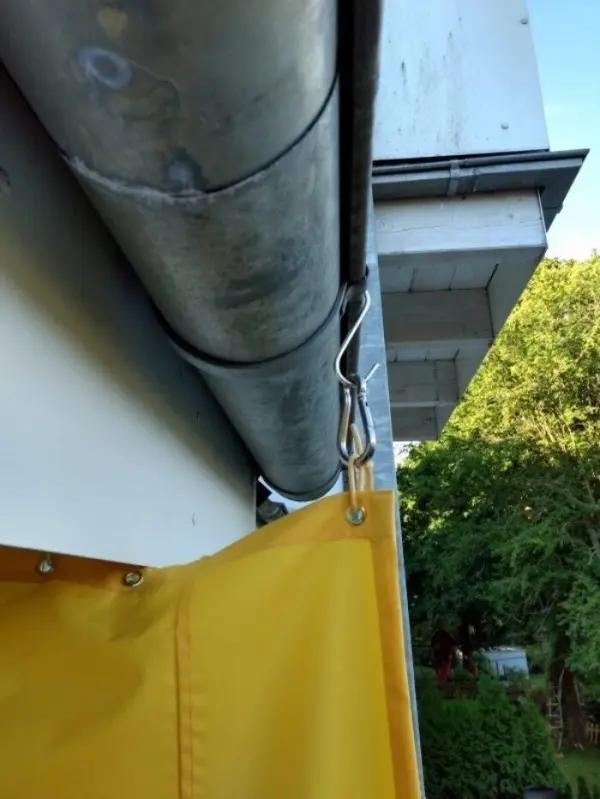 Ein gelbes Tuch hängt an einem Drahtseil, das an einer Metallröhre in einer grünen Umgebung befestigt ist.