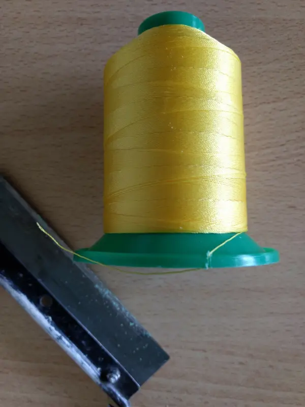 Ein Spulengarn in leuchtendem Gelb liegt neben einem Schneidewerkzeug auf einer Holzoberfläche, bereit zum Nähen für Sonnen- und Windschutz.