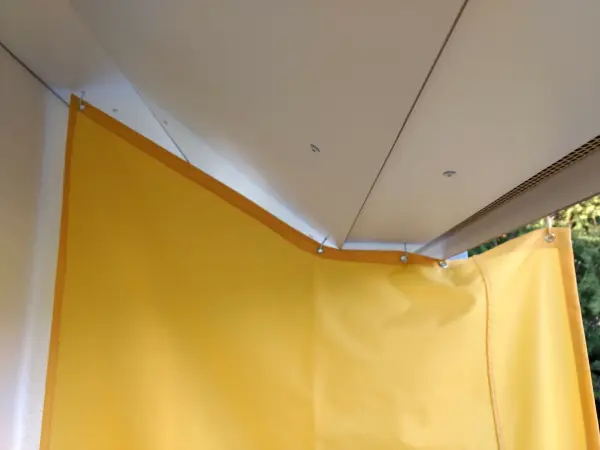 Ein gelber Windschutz hängt an der Decke und schützt den Raum vor Wind. Im Hintergrund sind Bäume sichtbar.