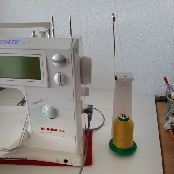 Eine Nähmaschine steht auf einem Tisch, bereit zum Nähen von Sonnen- und Windschutz, mit einer Spule gelber Faden daneben.