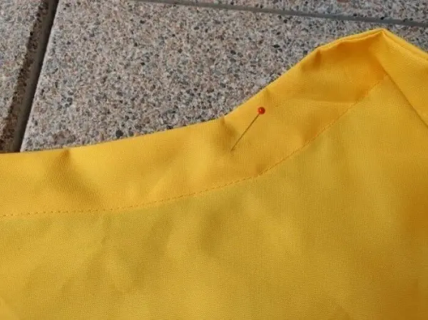 Ein gelbes Stoffstück liegt auf einem grauen Untergrund, mit einer Stecknadel, die den Stoff für den Nähprozess fixiert.