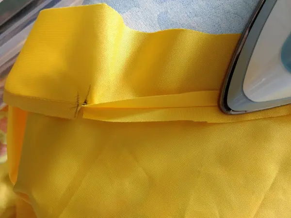 Ein hellgelbes Stück Stoff wird mit einem Bügeleisen bearbeitet, um Falten zu entfernen, während es auf einem Tisch liegt.