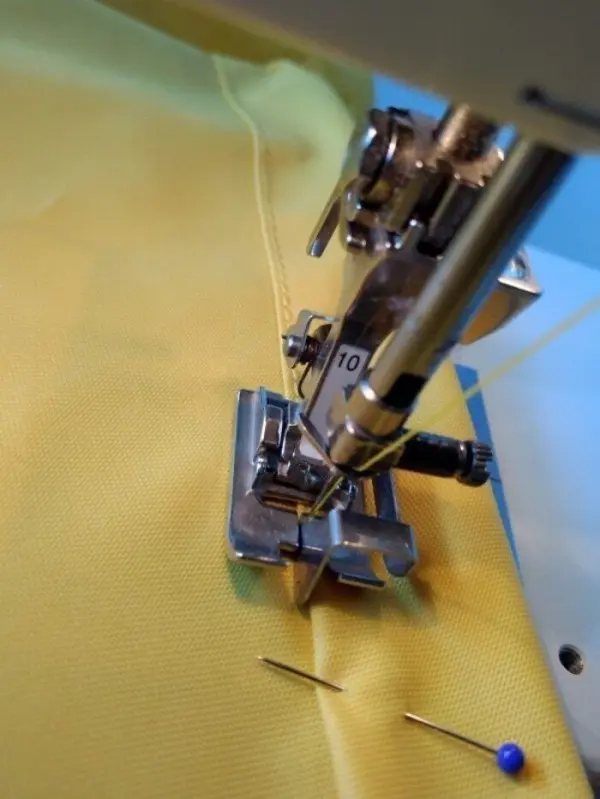 Eine Nähmaschine näht gelbes Material, während eine Nadel und Stecknadeln daneben liegen, um Sonnen- und Windschutz zu erstellen.
